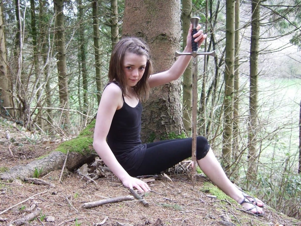 A young Maisie Williams poses with a sword in the woods during her early Game of Thrones audition days, foreshadowing her fierce portrayal of Arya Stark