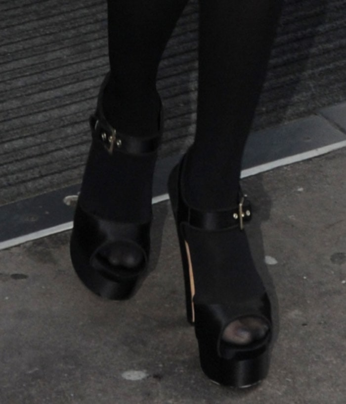 Brian Atwood’s black satin “Karin” sandals feature an open toe, buckled ankle strap, thick front platform, and towering block heel