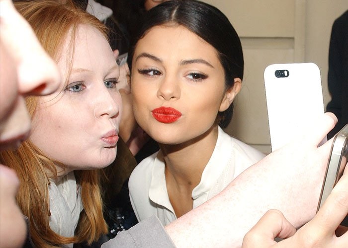 Gomez’s bold red lip becomes the focal point as she stops for a selfie, providing a strong beauty contrast to the otherwise all-white Paris ensemble
