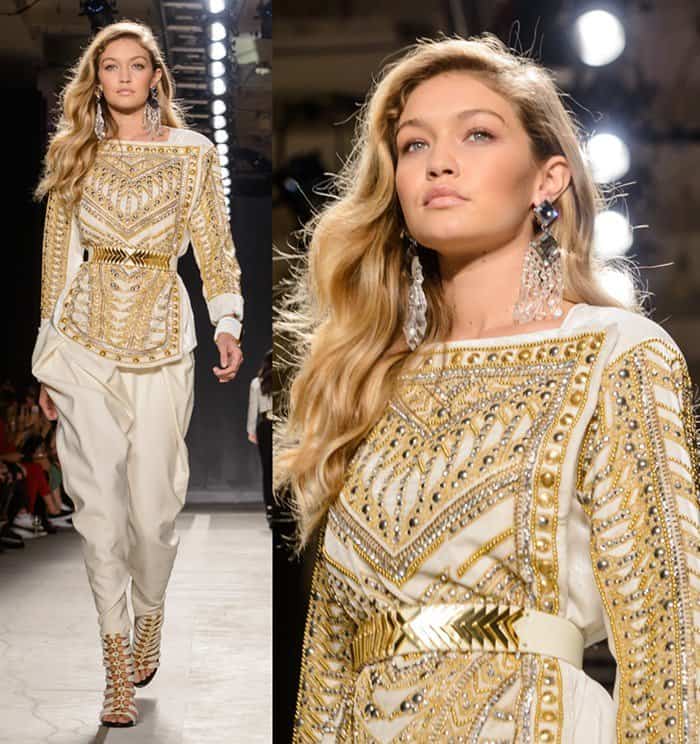 Gigi Hadid radiates on the runway in an opulent Balmain x HM ensemble featuring gold-embellished beadwork and a metallic belt, paired with strappy gladiator heels that add height and drama to her statuesque frame
