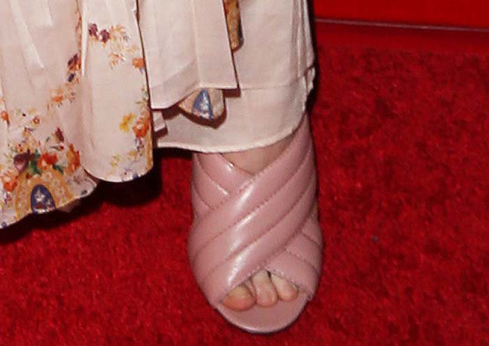 A close-up reveals Fanning’s blush-toned block-heel sandals, grounding the whimsical dress with a practical yet polished footwear choice