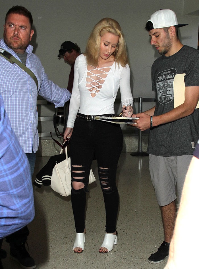 Iggy Azalea signs an autograph at LAX wearing a daring white lace-up Missguided bodysuit paired with ripped black jeans and white mule sandals