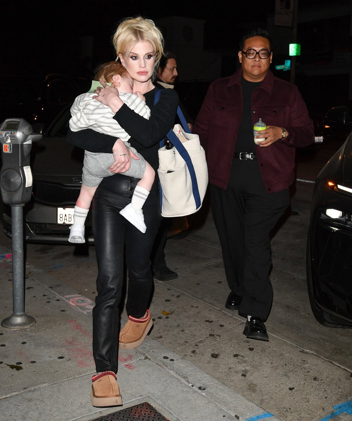 Kelly Osbourne carries her son while stepping out in black leather pants, a fitted sweater, and cozy platform UGG Tazz slippers at Craig's restaurant for best friend Daniel Nguyen's birthday celebration
