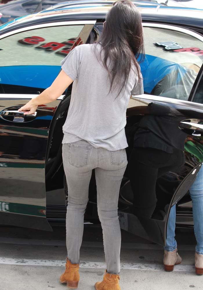Kourtney Kardashian is seen from behind in distressed gray skinny jeans and tan Saint Laurent Wyatt boots as she helps her kids into the car after ballet class
