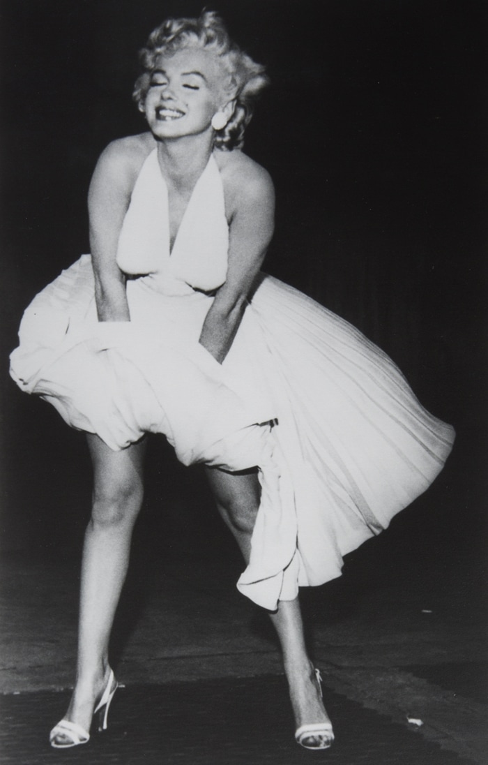 Bruno Bernard’s iconic black-and-white photo captures Marilyn Monroe in her billowing halter dress and strappy white stiletto sandals on the set of The Seven Year Itch, blending timeless glamour with playful sensuality