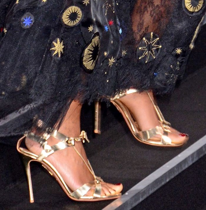 Naomie Harris flashes her metallic gold Aquazzura “Bel Air” sandals beneath the flowing hem of her embellished Valentino gown