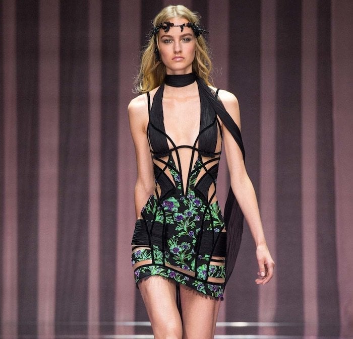 The Atelier Versace Fall 2015 runway version showcases the gown’s sculptural cutouts, floral embroidery, and dramatic scarf-like neck detail