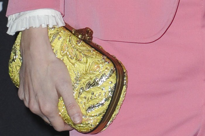 A close-up highlights Marling’s gold embroidered clutch, its ornate texture adding contrast and warmth to her pastel pink tailoring