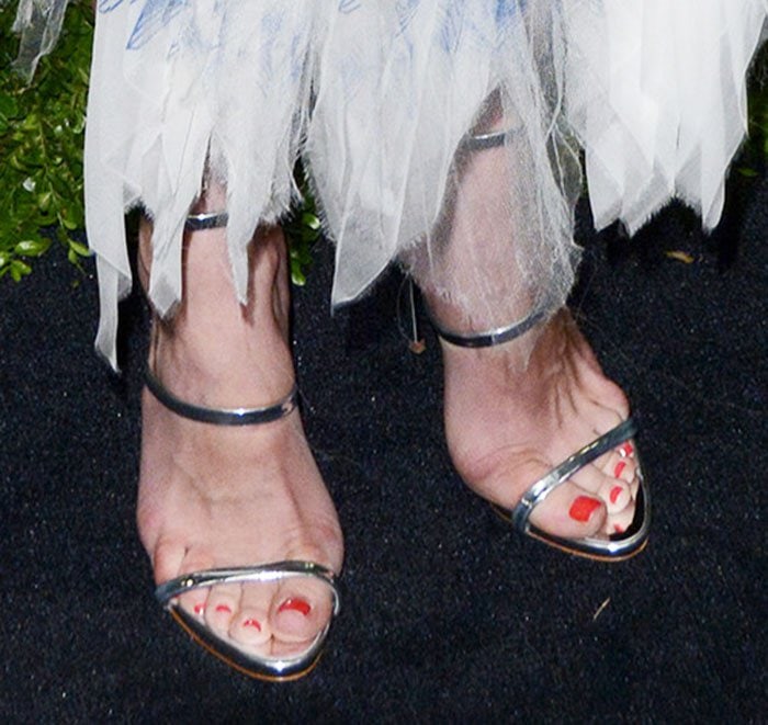 Her metallic Giuseppe Zanotti “Harmony” sandals—set on slender stiletto heels—bring a clean, reflective edge that sharpens the softness of the organza