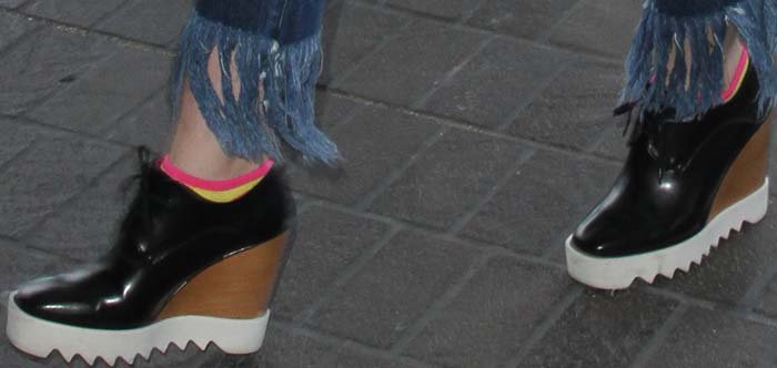 A close-up highlights Elle Fanning’s Stella McCartney wedge oxfords, featuring a glossy black upper, wooden wedge, and chunky white sawtooth sole for added height and stability