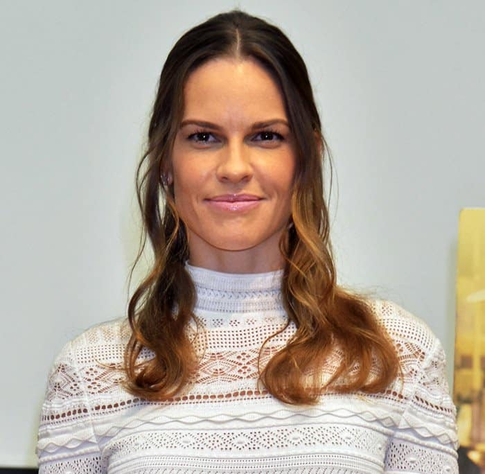 Hilary Swank’s beauty look perfectly complements her chic outfit with her soft, wavy hair parted down the middle, framing her face elegantly