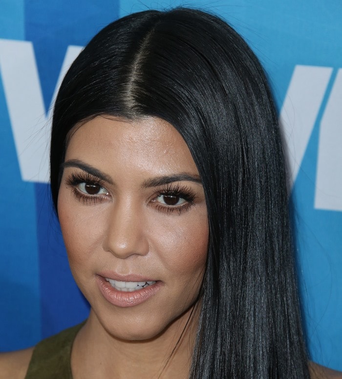 Kourtney Kardashian keeps her beauty look understated with center-parted, pin-straight hair, defined lashes, and a soft nude lip