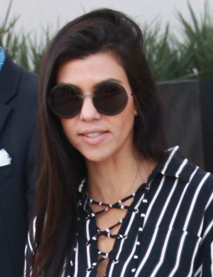 Kourtney Kardashian styles her long, dark hair down and accessorizes with oversized, round sunglasses for a sleek, effortless look