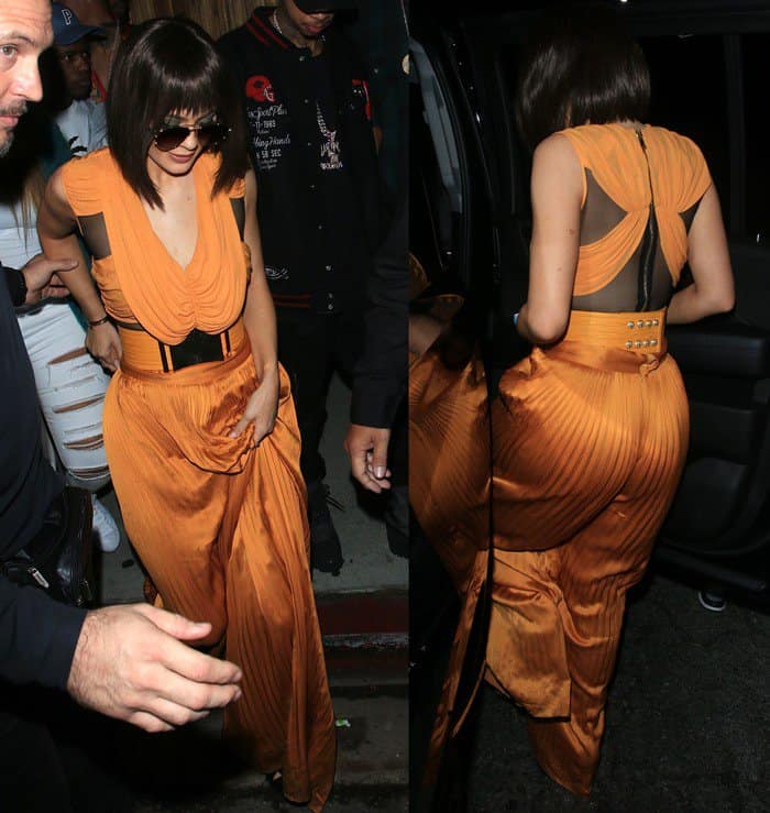 Kylie Jenner arrives at Kendall Jenner's 20th birthday celebration in a custom Balmain Fall 2015 pleated jumpsuit, styling the dramatic look with Dior So Real sunglasses, a wide patent-and-velvet Balmain belt, and sculptural Alaïa cutout suede boots