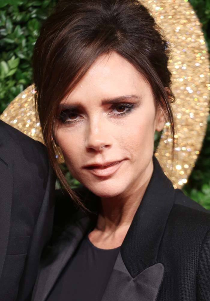 Victoria Beckham frames her signature smoky eye with a softly undone updo, adding a sultry beauty counterpoint to her razor-sharp black tailoring
