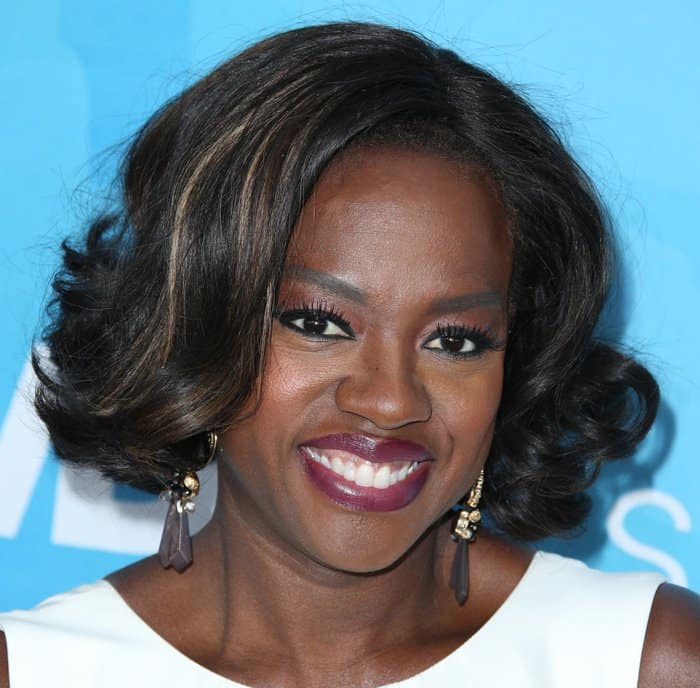 Viola Davis finishes her look with softly curled hair, smoky eye makeup, berry lipstick, and sculptural drop earrings