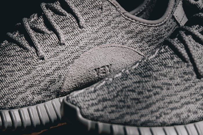 A close-up of the Adidas Yeezy Boost 350 "Moonrock" highlights the sneaker's marled Primeknit upper, suede side panel, and ribbed Boost sole, all rendered in the signature Agate Gray colorway