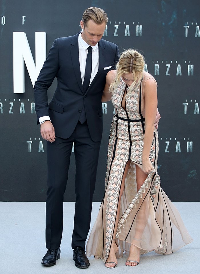 Margot Robbie bends down to adjust her Bally metallic “Eren” ankle-strap sandals at The Legend of Tarzan premiere, accidentally causing her intricately embroidered gown to unzip