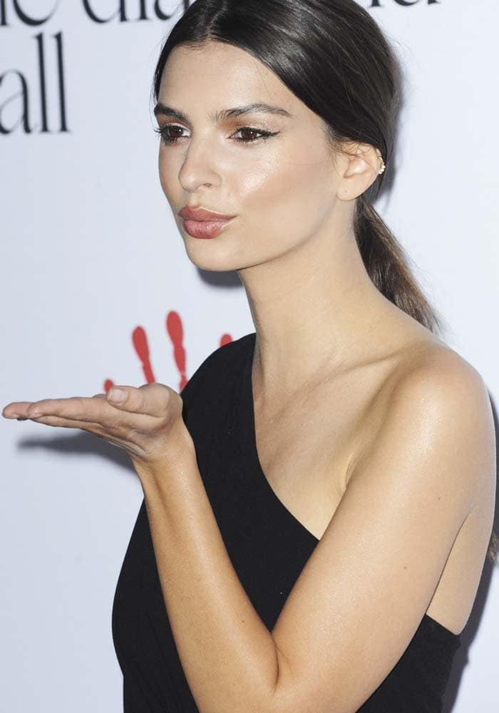 Emily Ratajkowski adds a playful note to her minimalist look, blowing a kiss while her sleek styling and sculpted silhouette maintain the evening’s refined, modern mood