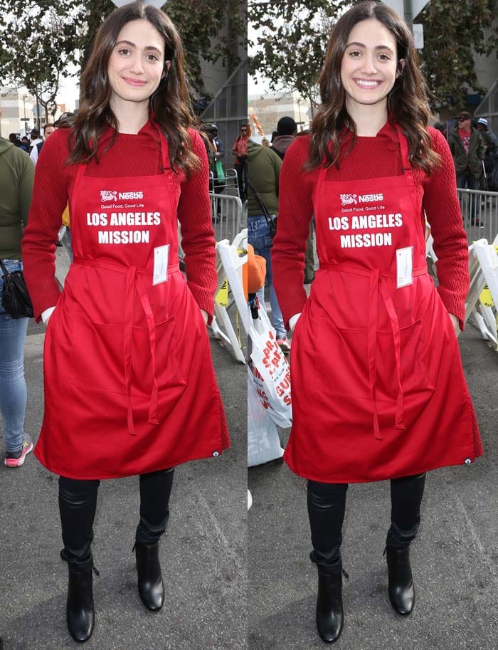 Layering a textured red sweater beneath her Los Angeles Mission apron, Emmy Rossum balanced warmth and polished simplicity with fitted black jeans and Prada boots