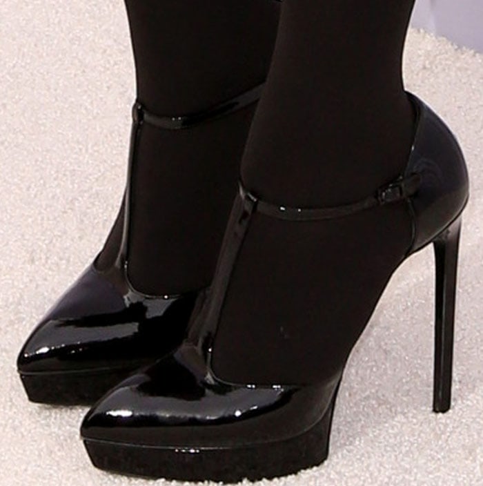 Kris Jenner makes a statement in glossy, black patent Saint Laurent pumps, featuring a striking T-strap design and a powerful platform base