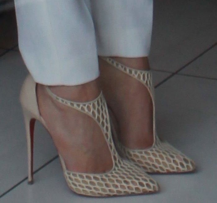 A close-up reveals the intricate fishnet construction and pointed toe of her Christian Louboutin pumps, emphasizing their illusion effect