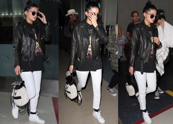 Kylie Jenner channels edgy airport chic in a black leather jacket layered over a vintage Yeezy tee, crisp white pants, and white Acne Studios sneakers that add a minimalist contrast to her monochrome palette