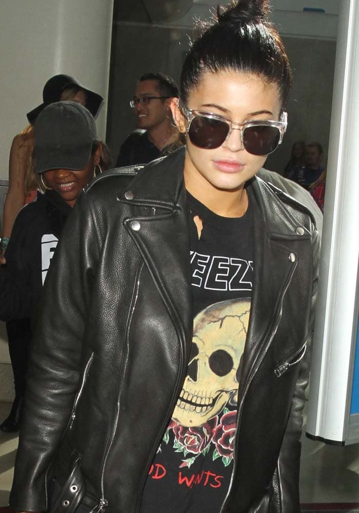 Kylie Jenner pairs a vintage Yeezy graphic tee with a sleek black leather biker jacket and oversized sunglasses, nailing her signature mix of edgy streetwear and understated luxury at LAX
