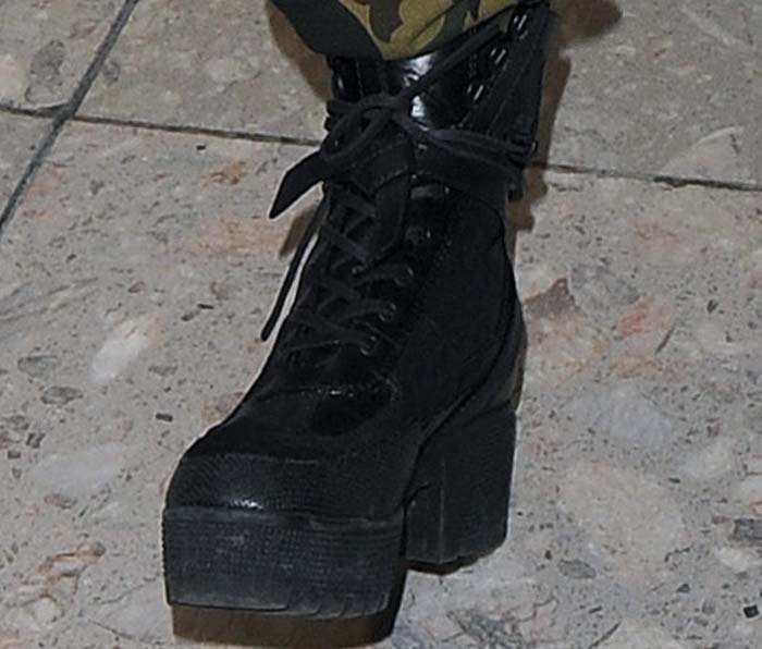A close-up highlights the rugged black platform boot, featuring a thick lug sole and block heel that add height and edge to Rita Ora’s travel outfit