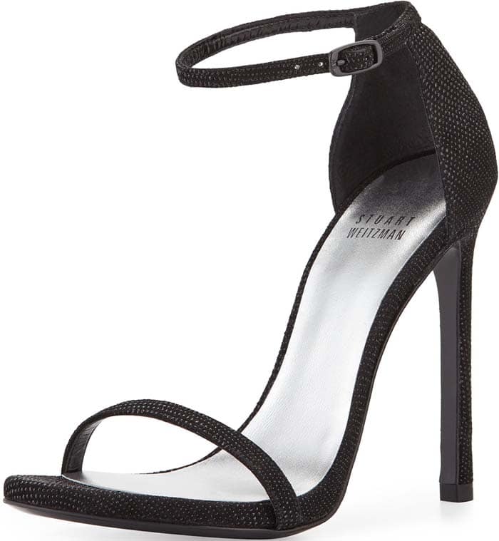 The Stuart Weitzman Nudist sandal in black Goosebump delivers a sleek, leg-lengthening effect with its barely-there straps, sky-high stiletto heel, and subtly textured finish
