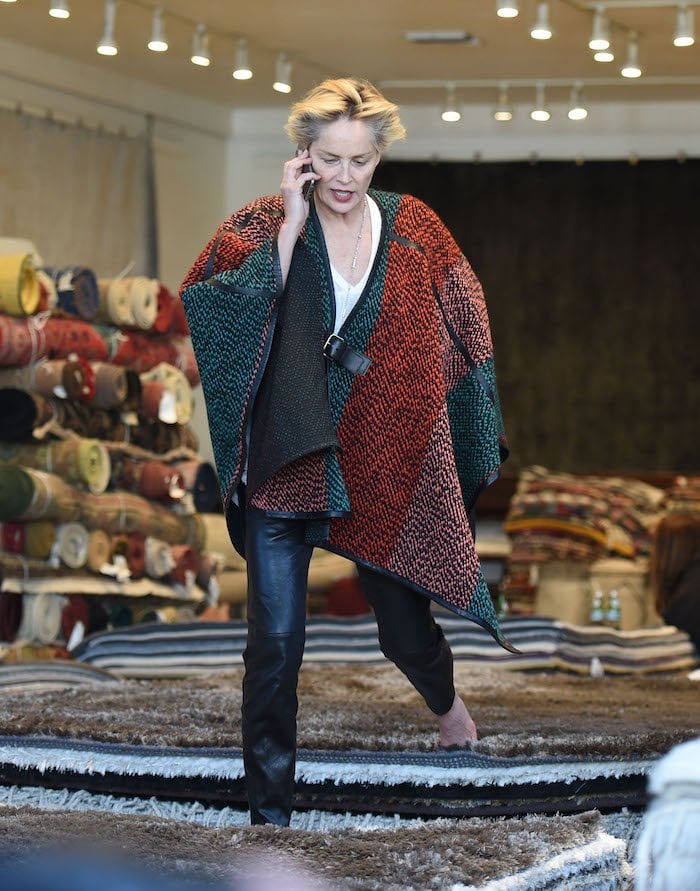 Sharon Stone takes her shoes off and tests out rugs while wearing a poncho