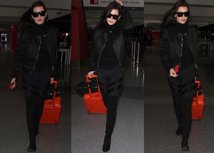 Bella Hadid makes airport dressing look effortlessly cool in an Acne Studios Fuel Tech bomber jacket, David Lerner Shine Twill Tribal leggings, Karen Walker Deep Freeze sunglasses, and her go-to Stuart Weitzman Lowland over-the-knee boots