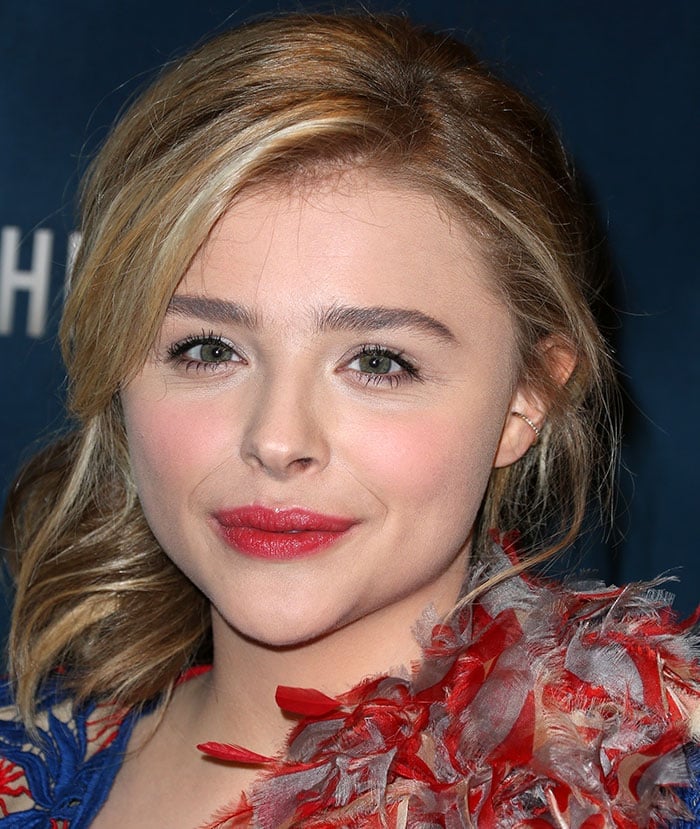 Chloë Grace Moretz dazzles with a bold red feathered accent and vibrant red lips, perfectly complementing her natural beauty and understated glam