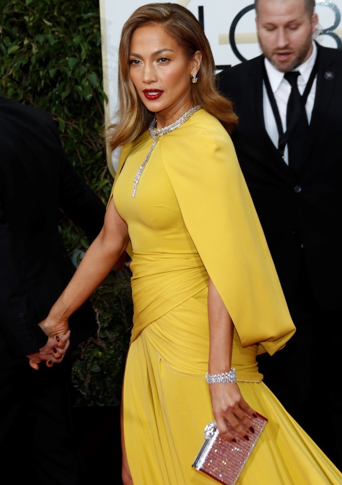 Seen from the side, Jennifer Lopez’s Giambattista Valli gown reveals its draped waist and cape-like overlay as she carries a crystal-encrusted Judith Leiber Couture clutch