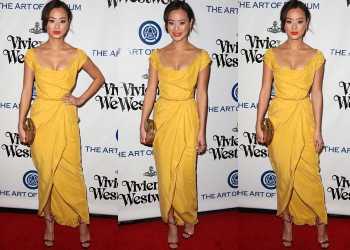 Jamie Chung brightens the red carpet in a draped gold Vivienne Westwood gown, styled with an Emm Kuo clutch and ruby-red Jimmy Choo sandals featuring sculptural cutout detailing