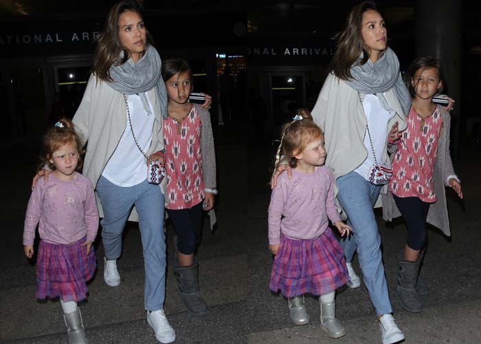 Jessica Alba with her daughters at the airport in 2016, wearing a casual yet stylish look with white sneakers, relaxed denim, and a cozy cardigan while guiding her children through the arrivals area