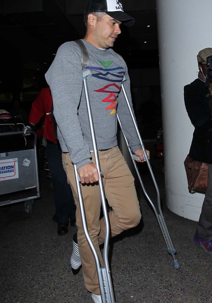 Cash Warren at the airport in 2016, navigating through the terminal on crutches after injuring his Achilles tendon, paired with a playful, colorful sweatshirt and stylish sneakers