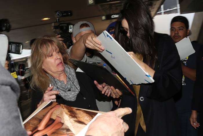 Kendall Jenner signs autographs for fans while making her way through a busy Los Angeles airport terminal