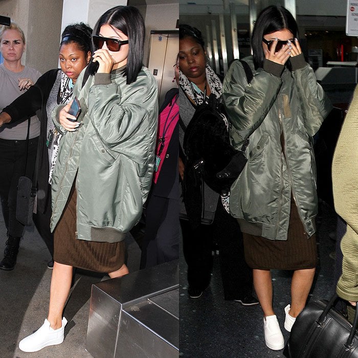 Kylie Jenner gives her airport look a utilitarian edge, grounding an oversized bomber jacket and midi skirt with crisp white sneakers