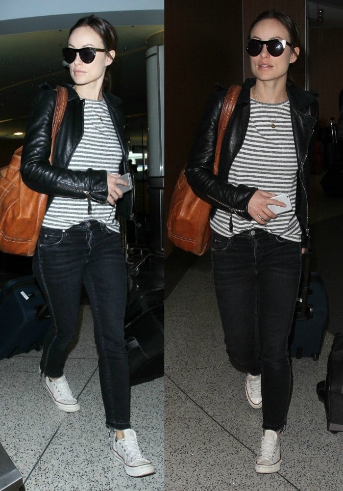 Olivia Wilde keeps it casual yet stylish in a striped tee, black leather jacket, skinny jeans, and classic white Converse sneakers, spotted at the airport with an effortlessly chic travel look