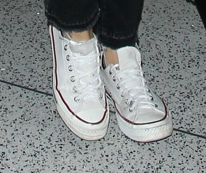 A close-up reveals Olivia Wilde’s footwear of choice—classic white Converse Chuck Taylor All Star sneakers grounding her casual travel outfit with timeless ease