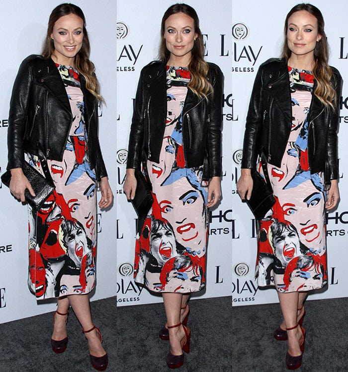 Olivia Wilde sharpens a playful Marc Jacobs pop-art midi with a black leather moto jacket and deep red platform Mary Jane heels that anchor the look with retro polish