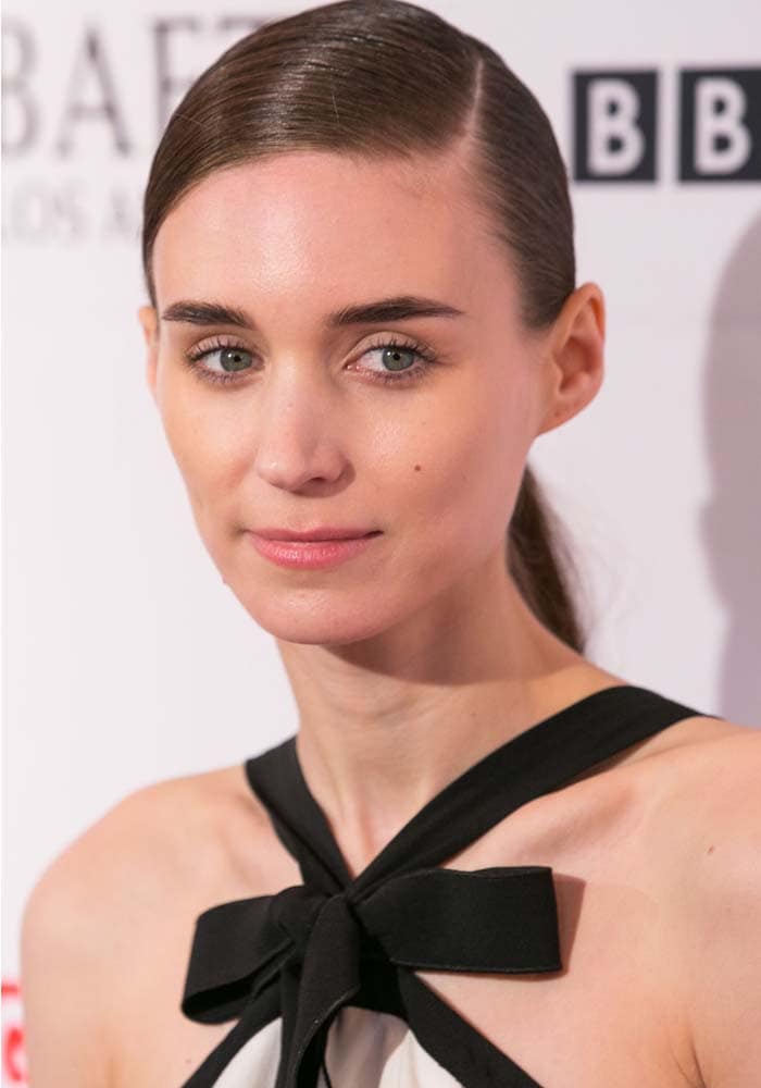 Rooney Mara keeps her beauty look minimal with softly defined eyes, a neutral lip, and sleek side-parted hair