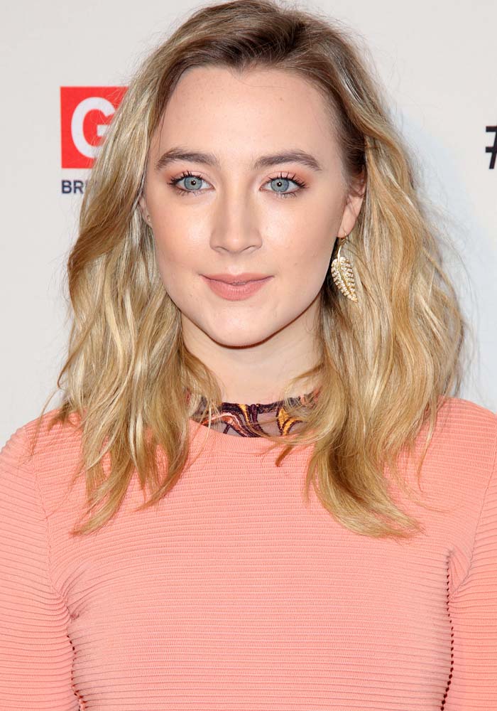 Saoirse Ronan with soft, tousled waves, subtle peach makeup, and a pair of gold leaf earrings that complement her peach dress