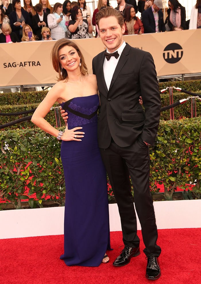 Sarah Hyland and Dominic Sherwood pose together on the SAG Awards red carpet as her fitted navy gown and his satin-lapel tuxedo create a polished black-and-blue evening pairing