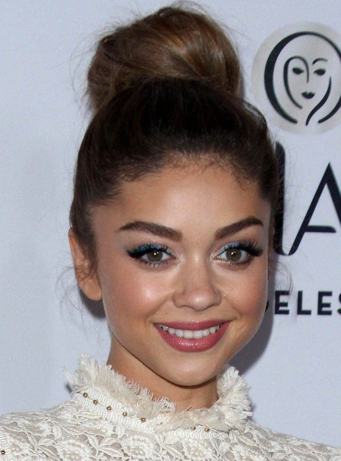 With a high topknot, winged liner, and soft glow, Sarah Hyland sharpens the sweetness of her lace dress with a clean, sculpted beauty look
