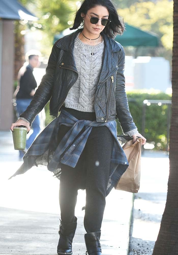 Vanessa Hudgens nails casual chic by layering a cable-knit sweater under a leather jacket, tying a flannel around her waist, and finishing the look with moto boots for effortless edge