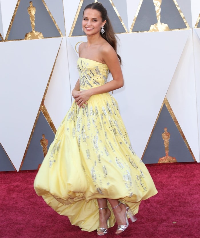 Alicia Vikander dazzles in a custom yellow Louis Vuitton gown with silver embellishments at the 2016 Academy Awards, completing the look with metallic lucite heels