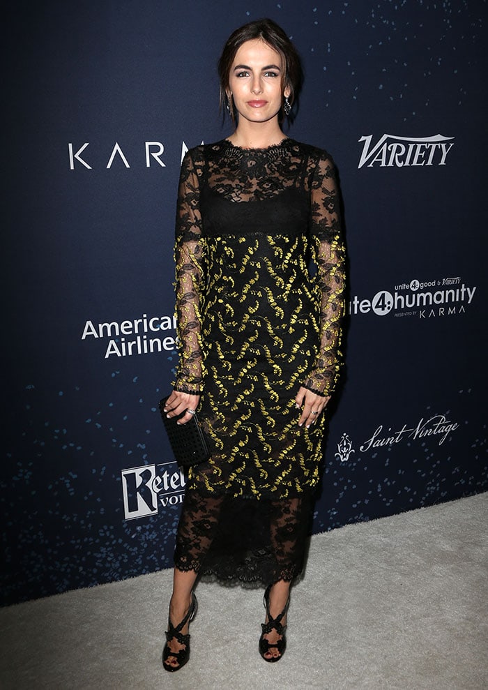 Camilla Belle balances gothic romance and modern edge in a sheer black lace Monique Lhuillier dress, finished with sculptural Christian Louboutin “Decoupadiva” heels at the Unite4:Humanity event