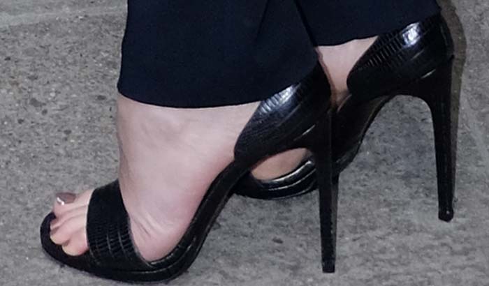 A close-up reveals Dakota Johnson’s black reptile-embossed Saint Laurent “Jane” sandals featuring slim ankle straps and towering stiletto heels